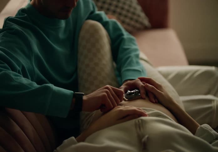 Father cranks a music box on his pregnant wifes abdomen in their living room