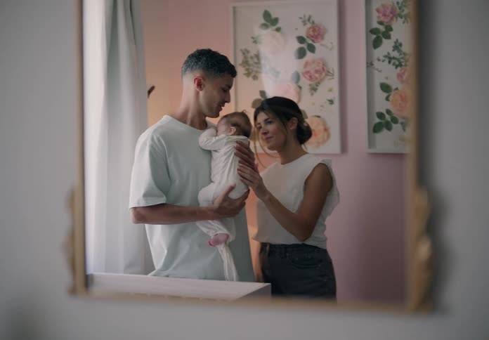 Reflection in a mirror of a young couple cradling a newborn baby