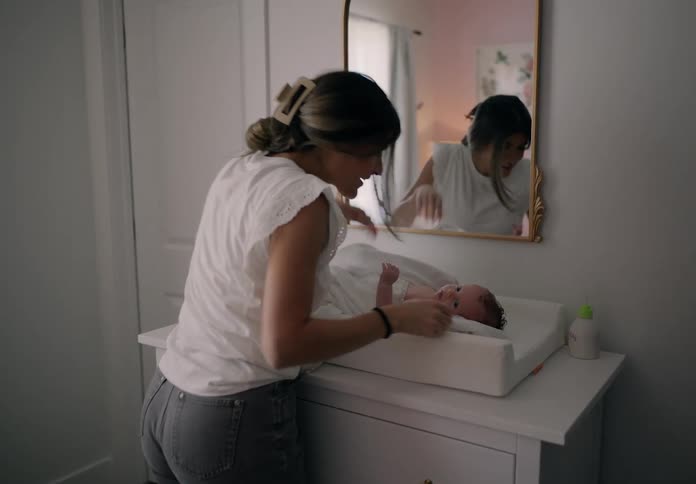 A mother carries a baby into the bedroom to change the diapers