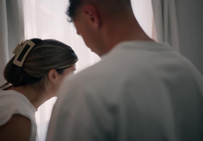 A man picking up a newborn baby and placing him in his crib and on the way he gives him a kiss on the cheek and a woman too and they are happy