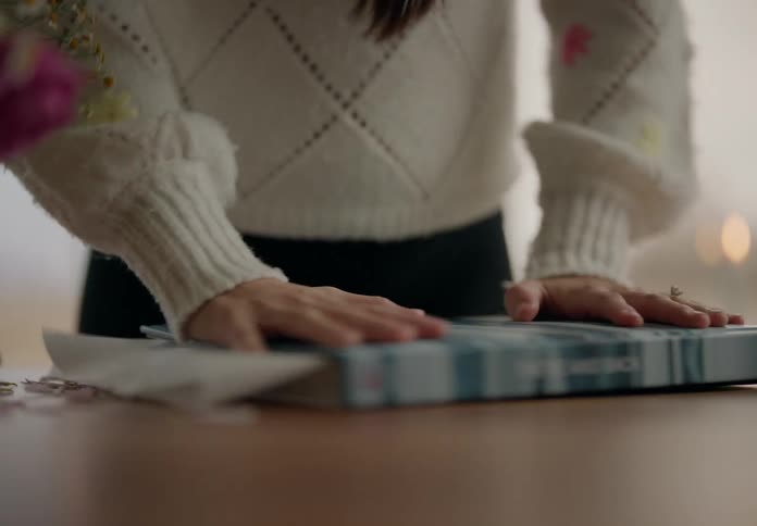 A human hand closing a book with some flowers inside it and she is crushing them with the cover