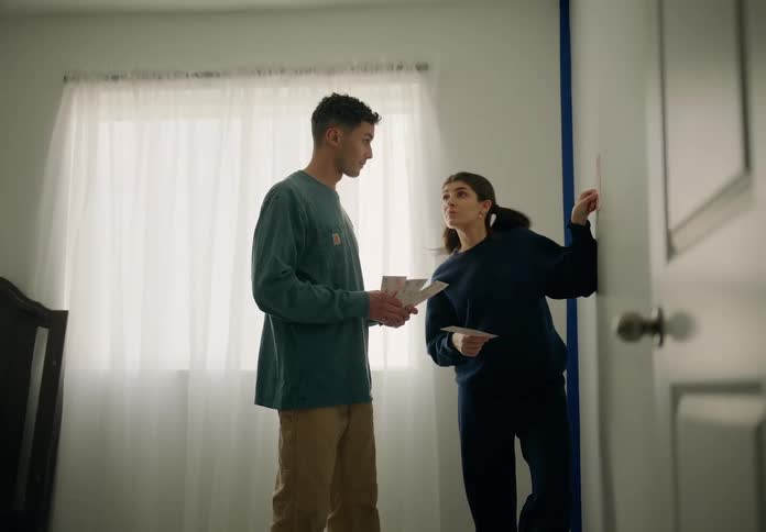 Couple in bedroom talking to each other and holding framed cards