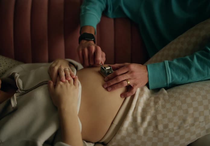 Man turning a toy crank on the belly of a pregnant woman who is lying next to him