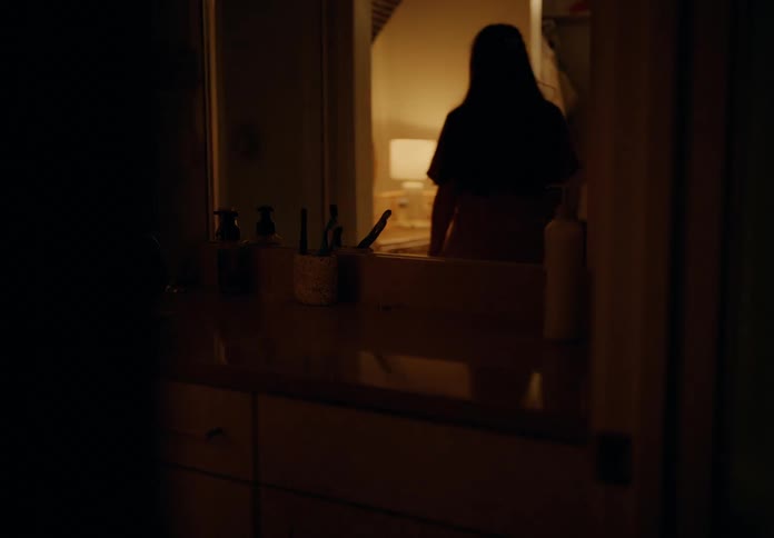 Reflection of a woman sitting at a night table in a dimly lit room
