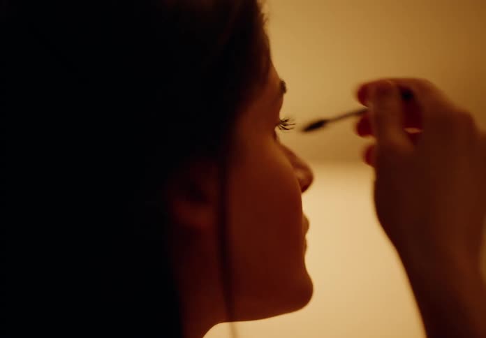 Woman sits inside applying makeup with a wand