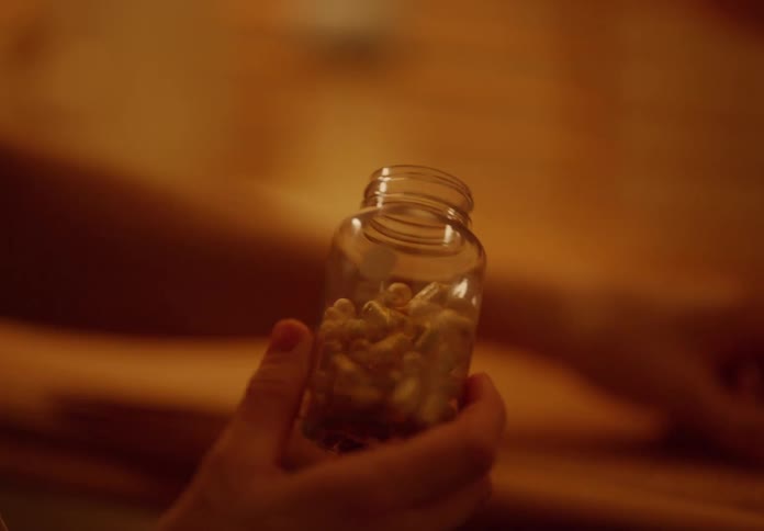 Person picking up a small jar opening it taking out a capsule and closing it again