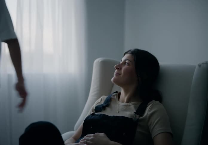 A woman is sitting in a chair and then a man comes and kisses her on the forehead
