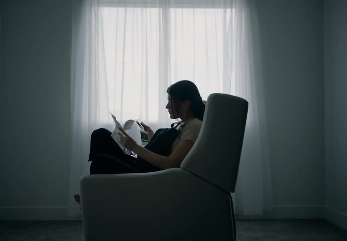 A pregnant woman sitting in a chair by a window with sheer curtains looking at echo sonograms