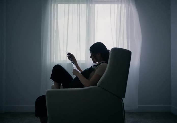 A pregnant woman sitting in a chair by a window with sheer curtains looking at echo sonograms