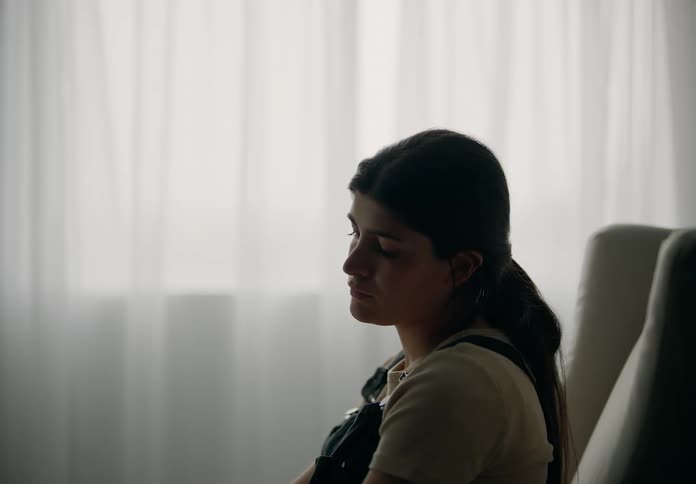 A young woman sitting in an armchair and behind her there is a white curtain of a window