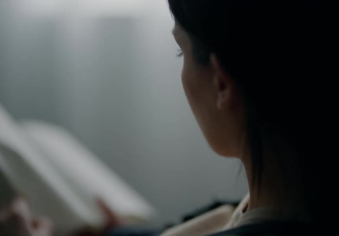 Close up of the profile of a woman reading a book on a dimly lit room