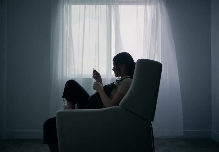 A pregnant woman sitting in a chair by a window with sheer curtains looking at echo sonograms
