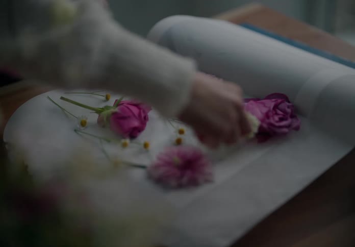 A human hand placing some pink petal flowers on top of a white paper