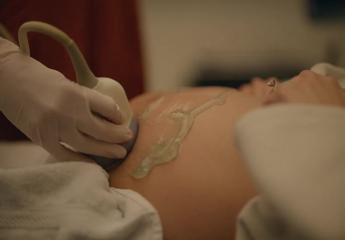 Hand with glove holding a device on the belly with gel of a pregnant woman