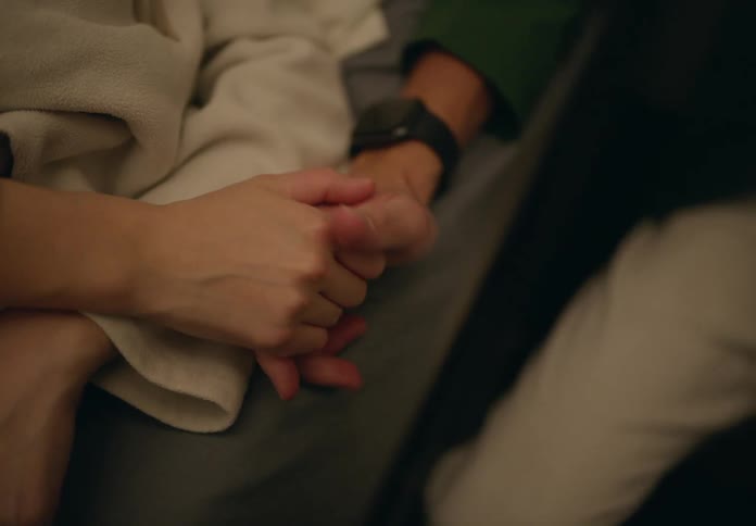 Man sitting next to a pregnant woman lying down with their hands clasped together