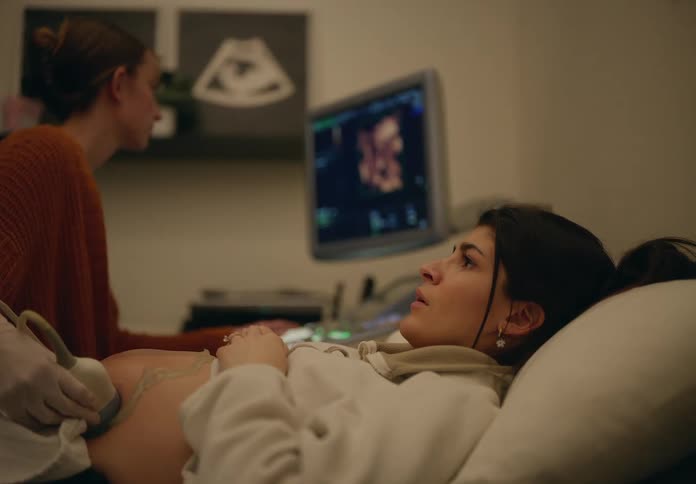 A pregnant woman lying in a bed in a medical office as a female doctor performs a sonogram on her