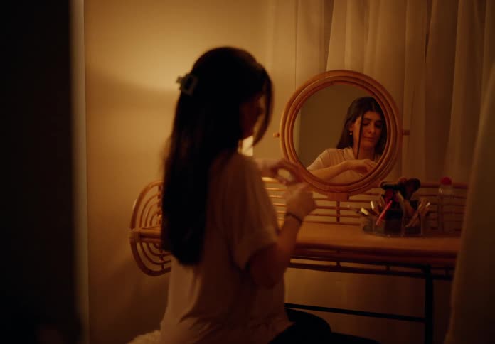 Woman sitting in a room facing a mirror taking medicine and removing her earrings