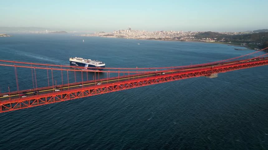 Aerial view of a red bridge above the sea with a cargo ship in the background