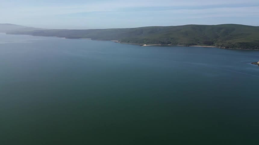 A large bay of blue water is on the coast large green hills and a small island in the center