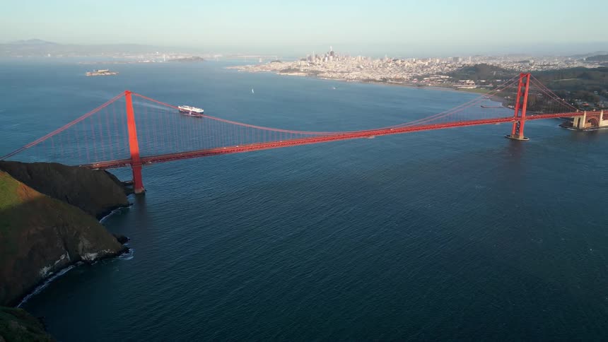 Aerial view of a red bridge connecting mountains above the sea with the metropolis in the background