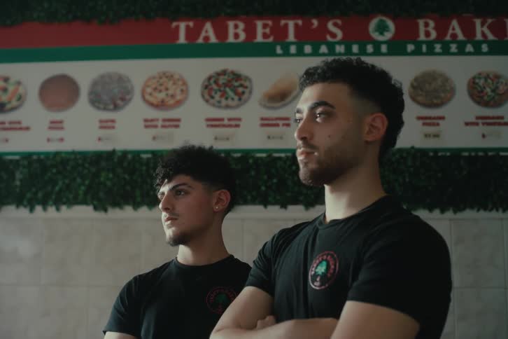 Two young men standing in front of a menu board at tabets bakery a lebanese pizza restaurant