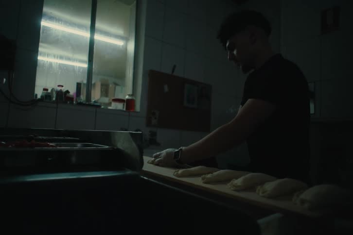 A person in a dimly lit kitchen focused on preparing food on a wooden surface