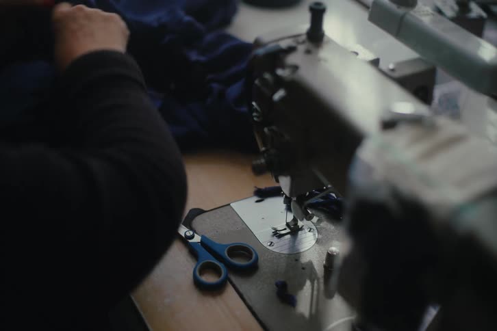 A human hand using scissors to cut a piece of clothing and next to it is a sewing machine