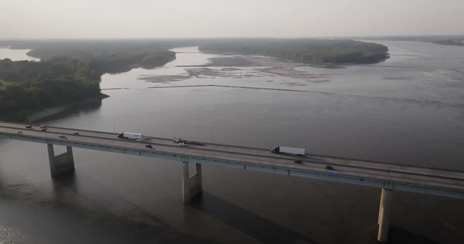 Aerial view of a long bridge with heavy traffic crossing a wide river