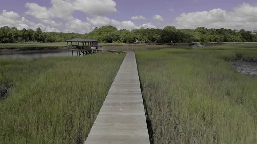 Aerial view of a long wooden boardwalk extending through a grassy marshland towards a gazebo