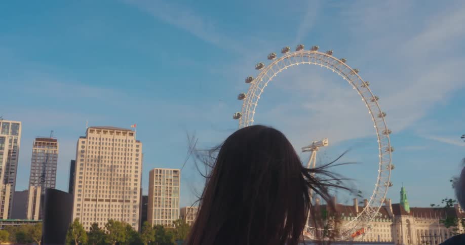 A view of the london eye from behind a person with long hair while riding a tour bus