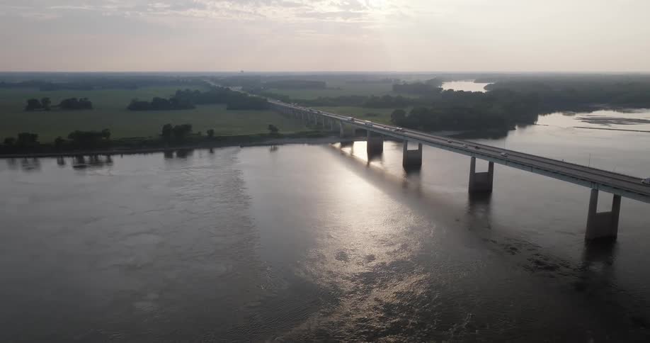 A freeway bridge crossing a large river with cars and a truck driving through it