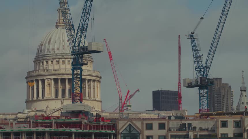 Some blue and red construction cranes stand in front of a historic domeshaped building