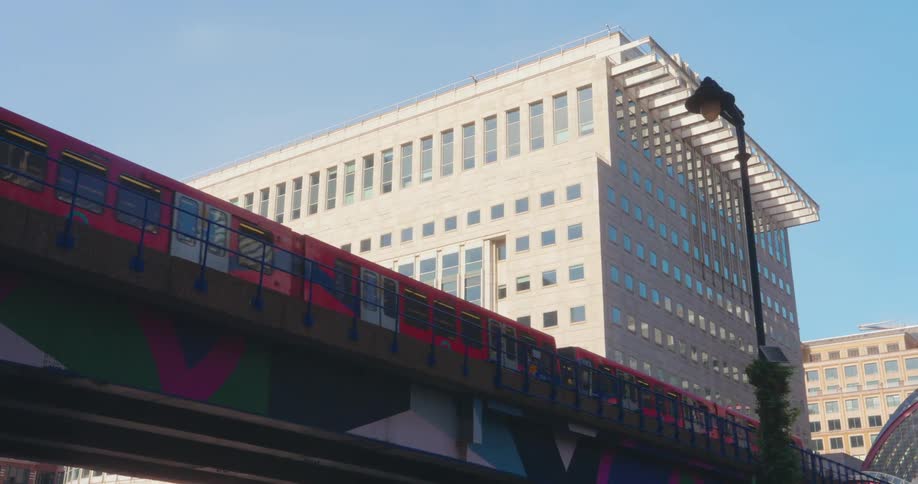 A colorful train crosses a geometricpatterned bridge in an urban area with buildings in the background