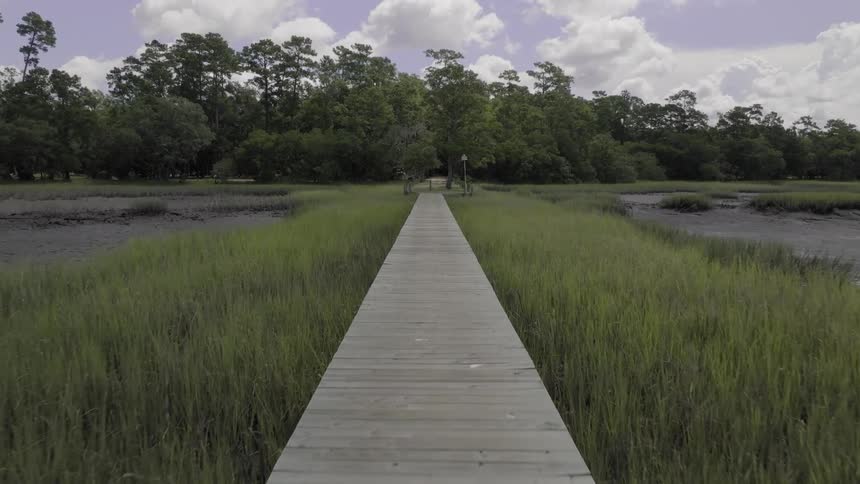 Aerial view of a long wooden boardwalk extending through a grassy marshland towards a gazebo