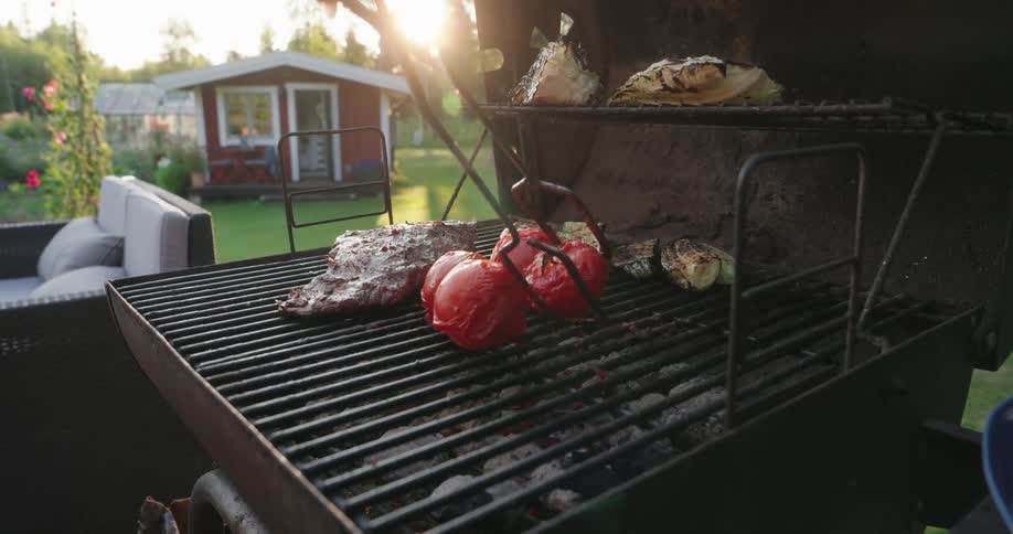 A closeup view of a barbecue grill with steak and vegetables cooking