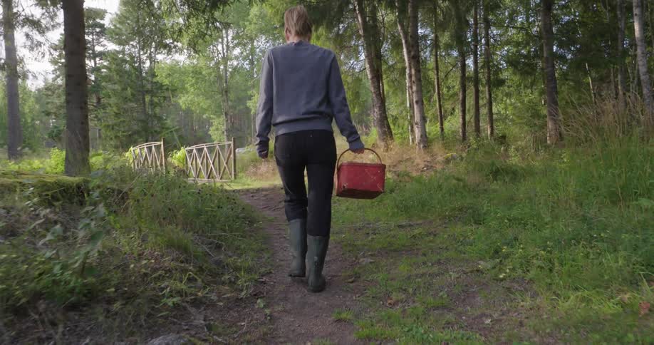 A woman carries a red wicker basket through the forest collecting mushrooms