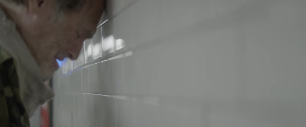 An old man leans his head against a tiled walled
