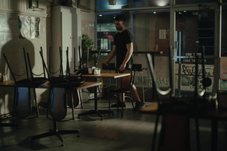 Man arranging chairs in a restaurant at night