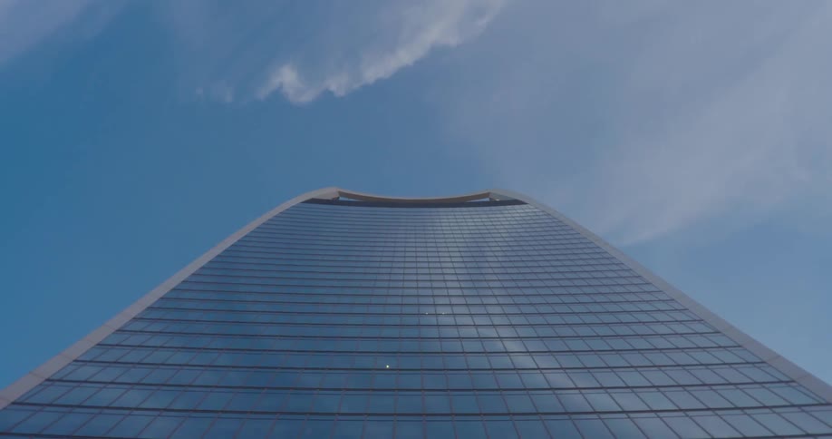 Upward view of a mirrored skyscraper against a blue sky