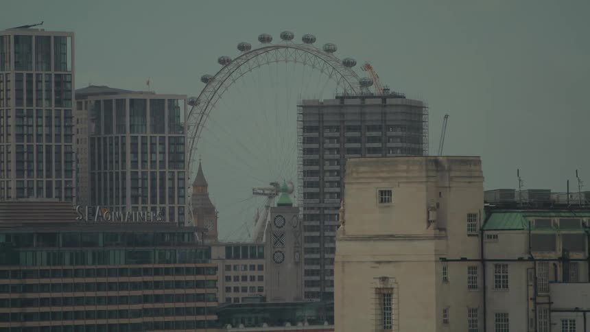 A shot of a city skyline with an observation wheel behind the buildings
