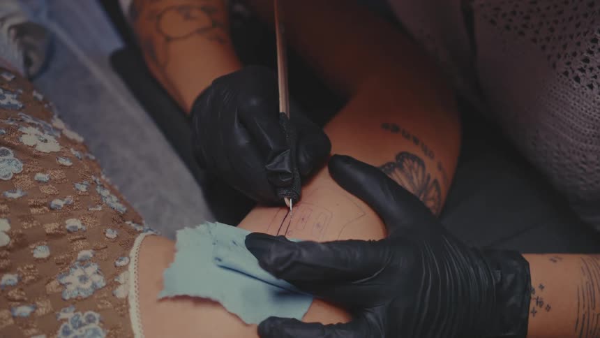 Hand with gloves performing tattoo on a persons arm