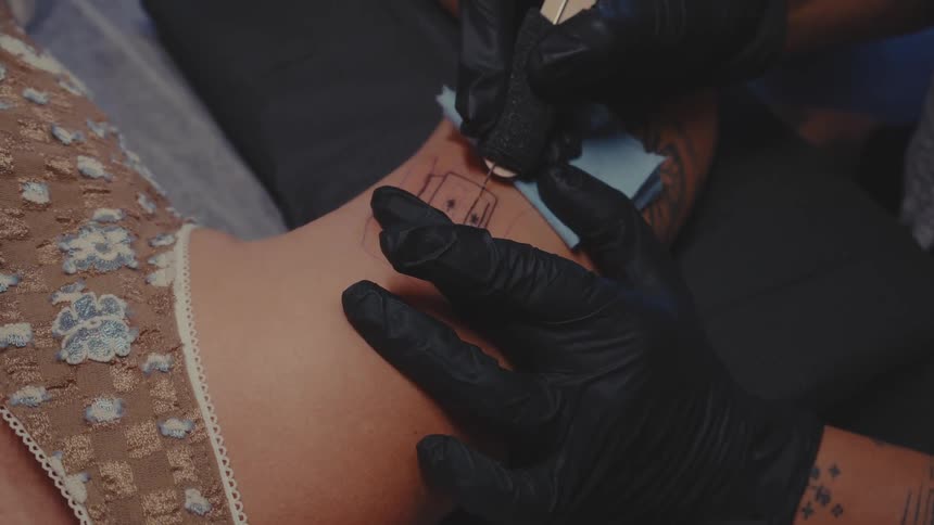 A person receiving a tattoo on their arm from a tattoo artist wearing black gloves