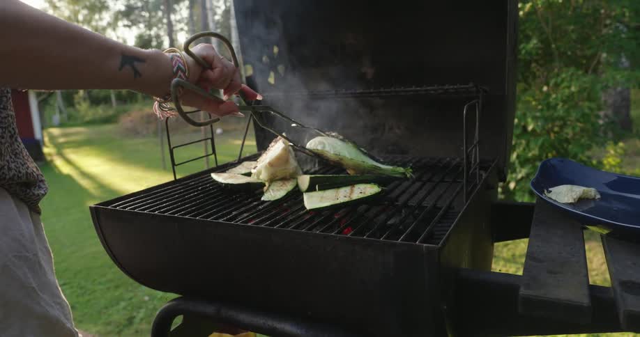 A woman is flipping vegetables on a barbecue