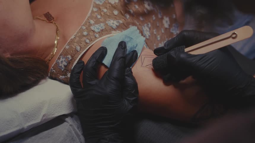 A person receiving a tattoo on their arm from a tattoo artist wearing black gloves