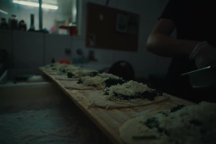 Close up of the hands of a person preparing food on a dimly lit kitchen at a restaurant