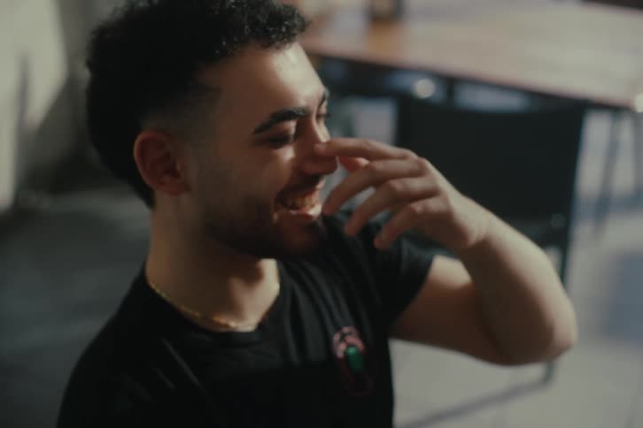 A young man sits at a cafe table talking to a friend smiling and laughing