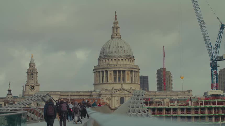 View of st pauls cathedral in london with a cloudy sky in the background and pedestrians on the bridge