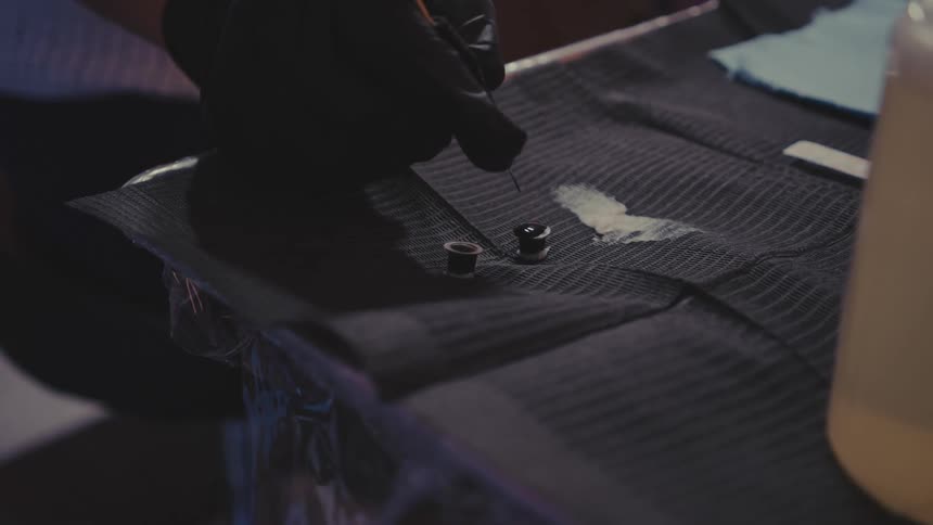 Human hands with black gloves applying a drop of black liquid on top of a small metal object