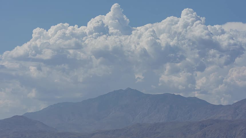 A rugged mountain range silhouetted against a vast sky filled with billowing cumulus clouds