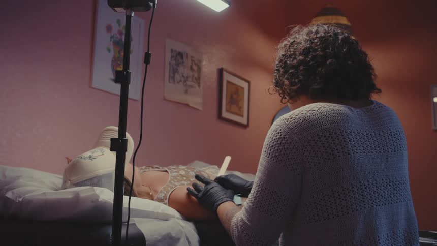 A person receiving a tattoo on their arm from a tattoo artist wearing black gloves